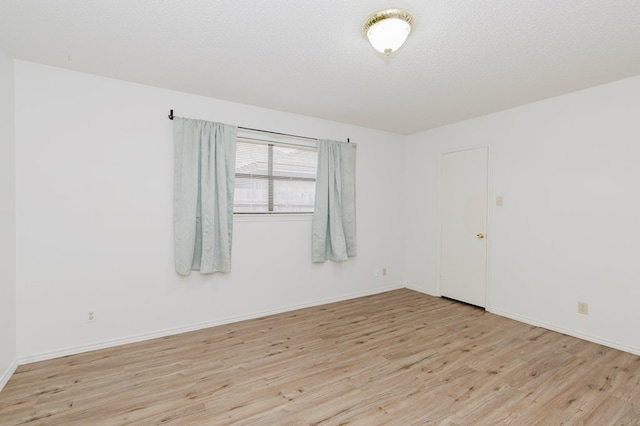 spare room with baseboards, a textured ceiling, and light wood-style flooring