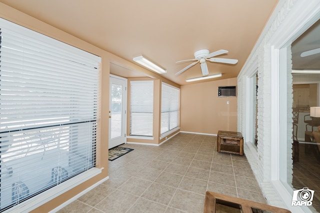 sitting room with light tile patterned flooring, a wall unit AC, a ceiling fan, and baseboards