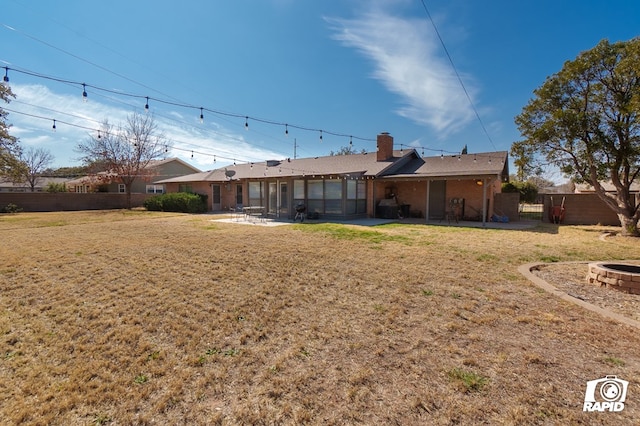 back of property featuring a patio, a chimney, a lawn, fence, and a fire pit