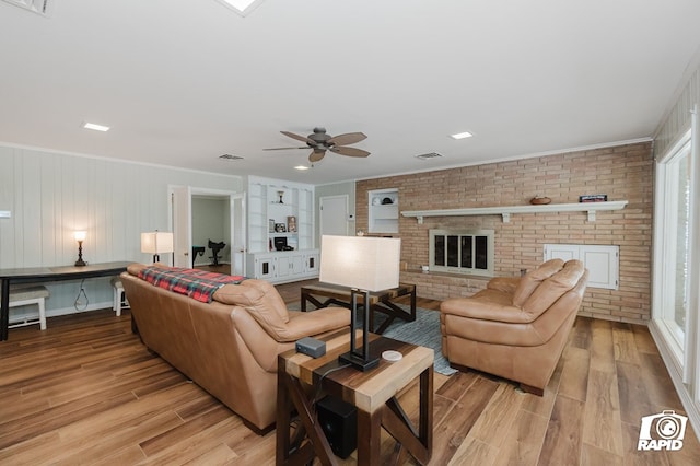 living room with brick wall, a fireplace, visible vents, ornamental molding, and light wood-type flooring