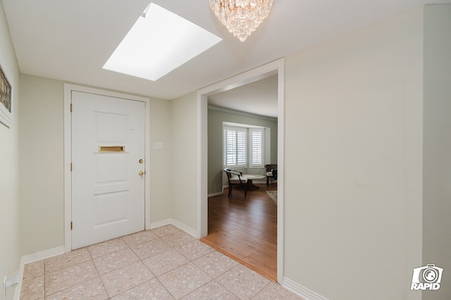 foyer entrance with a skylight, a notable chandelier, baseboards, and light tile patterned floors