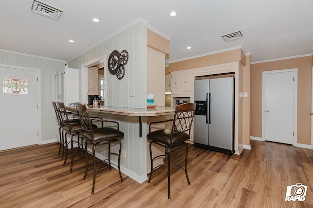 kitchen featuring light countertops, a breakfast bar, visible vents, and stainless steel refrigerator with ice dispenser