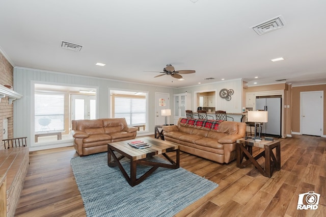 living area with a brick fireplace, visible vents, wood finished floors, and ornamental molding