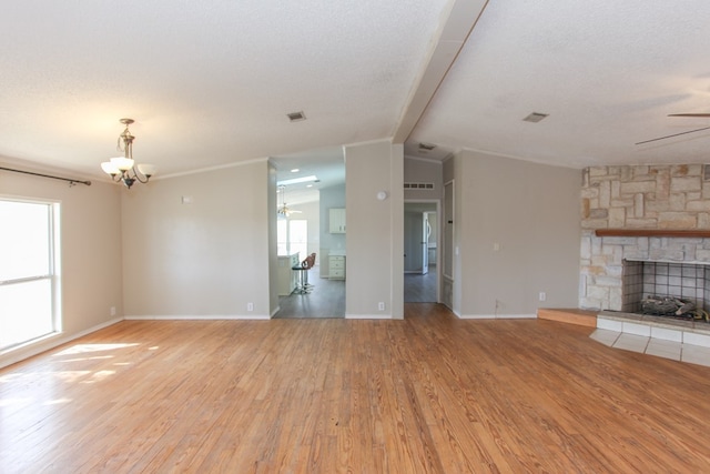 unfurnished living room with ceiling fan with notable chandelier, a stone fireplace, vaulted ceiling with beams, a textured ceiling, and light hardwood / wood-style floors