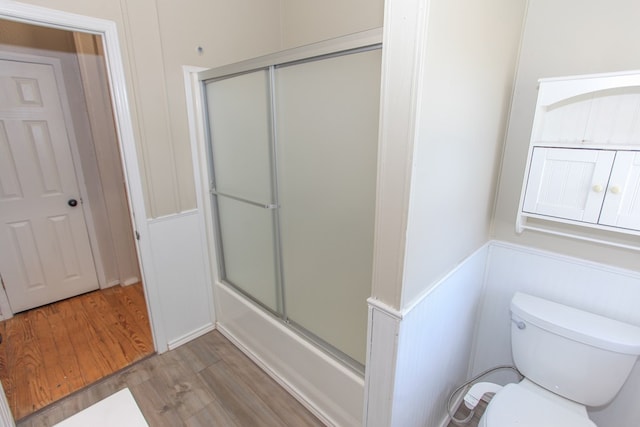 bathroom with hardwood / wood-style flooring, toilet, and bath / shower combo with glass door