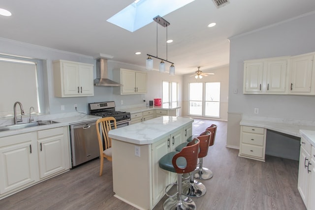 kitchen with ceiling fan, a center island, sink, stainless steel appliances, and wall chimney range hood