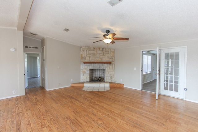 unfurnished living room with a textured ceiling, vaulted ceiling, ceiling fan, a fireplace, and light hardwood / wood-style floors