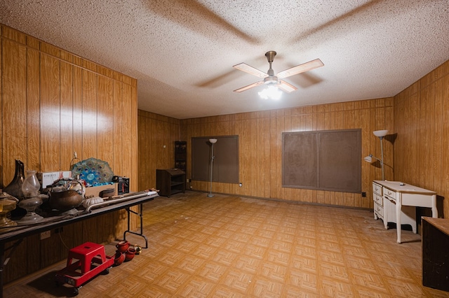 home office featuring wooden walls, light parquet flooring, ceiling fan, and a textured ceiling