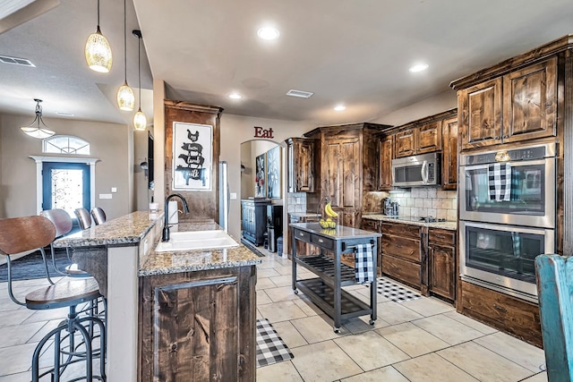 kitchen with sink, appliances with stainless steel finishes, decorative light fixtures, light stone counters, and kitchen peninsula