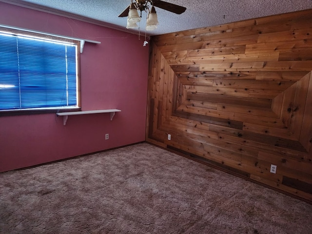 spare room featuring carpet flooring, a textured ceiling, ceiling fan, and wood walls