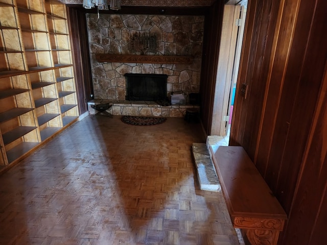 living room with parquet flooring, a stone fireplace, and wooden walls