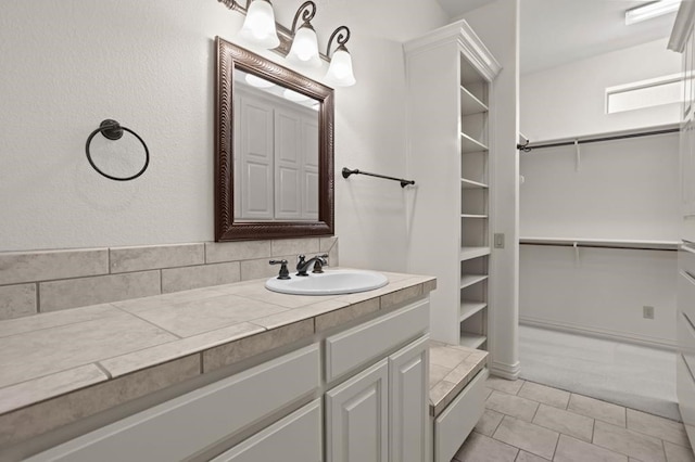 bathroom with a walk in closet, vanity, and tile patterned floors