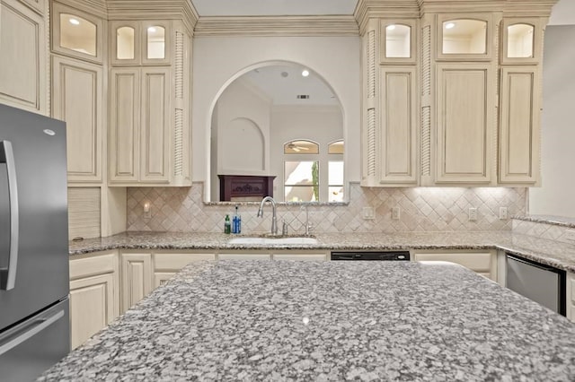 kitchen with light stone counters, a sink, cream cabinetry, freestanding refrigerator, and crown molding