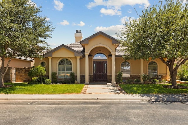 mediterranean / spanish-style house featuring a tile roof, a chimney, a front lawn, and stucco siding