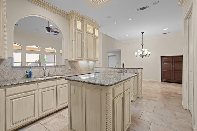 kitchen featuring visible vents, decorative backsplash, cream cabinets, a sink, and ceiling fan with notable chandelier