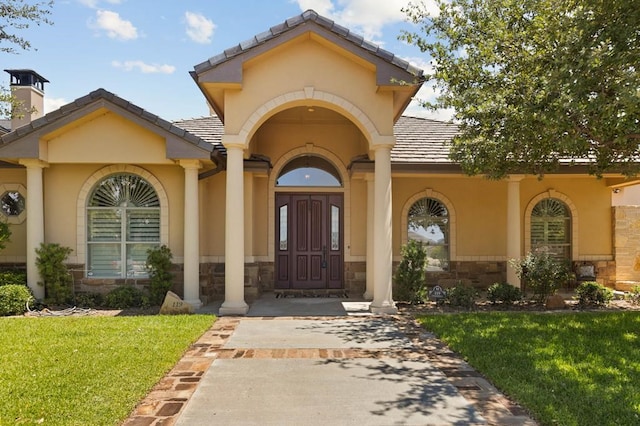 doorway to property with stone siding, a lawn, and stucco siding