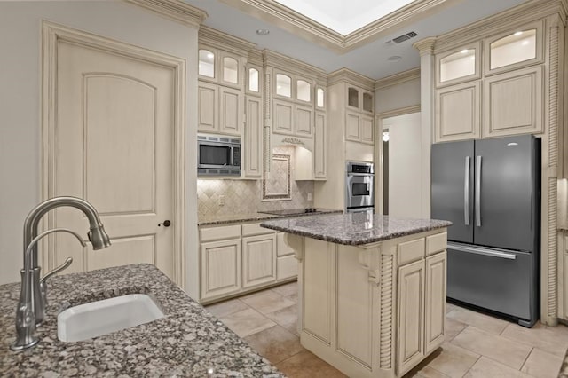 kitchen with dark stone counters, a kitchen island, cream cabinets, stainless steel appliances, and a sink