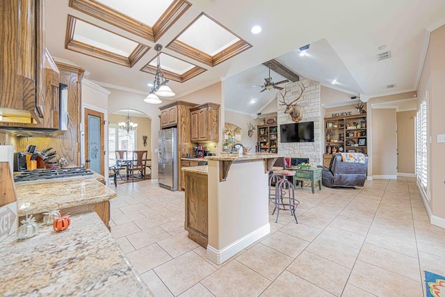 kitchen with light stone countertops, a breakfast bar, ceiling fan with notable chandelier, stainless steel appliances, and vaulted ceiling with beams