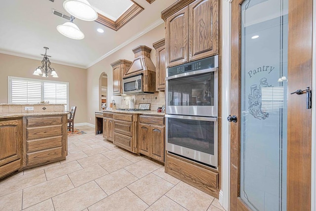 kitchen with an inviting chandelier, backsplash, crown molding, light tile patterned flooring, and appliances with stainless steel finishes