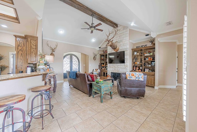 tiled living room with beam ceiling, a stone fireplace, ceiling fan, and crown molding