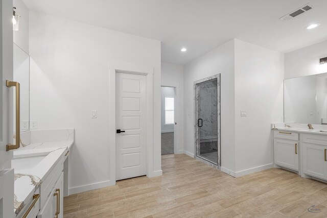 full bathroom featuring wood finished floors, a stall shower, two vanities, and visible vents