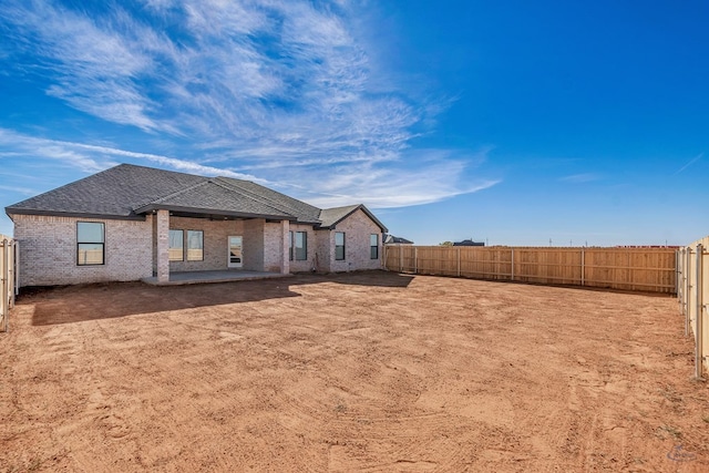 back of house featuring a fenced backyard, brick siding, and roof with shingles