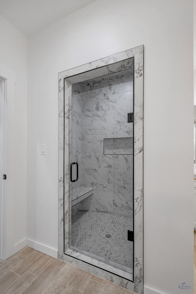 full bath with wood tiled floor, a marble finish shower, and baseboards