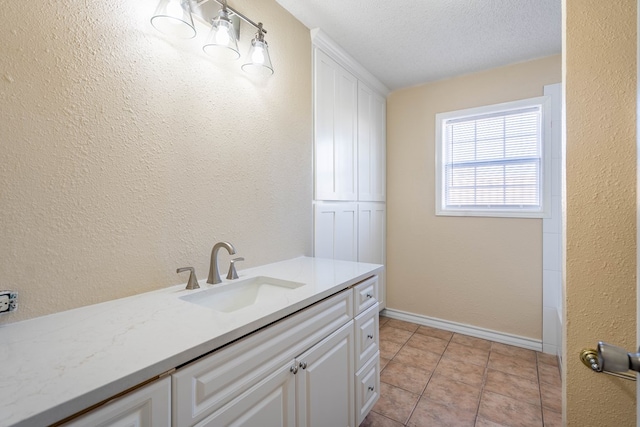 laundry area featuring a sink, a textured ceiling, light tile patterned flooring, baseboards, and a textured wall