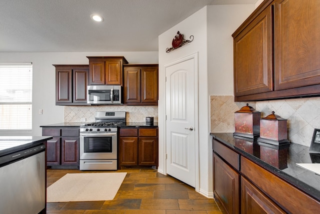 kitchen featuring dark wood finished floors, recessed lighting, decorative backsplash, appliances with stainless steel finishes, and dark stone counters