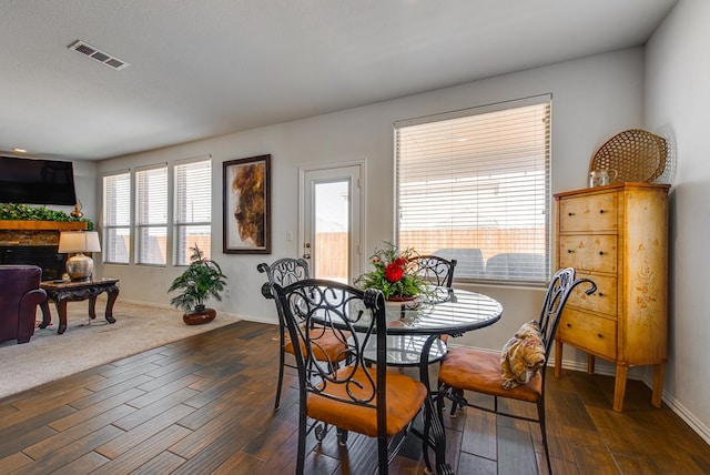 dining area with baseboards, a fireplace, visible vents, and dark wood finished floors