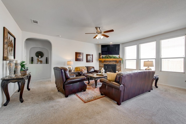 living room with a stone fireplace, a ceiling fan, visible vents, and light colored carpet