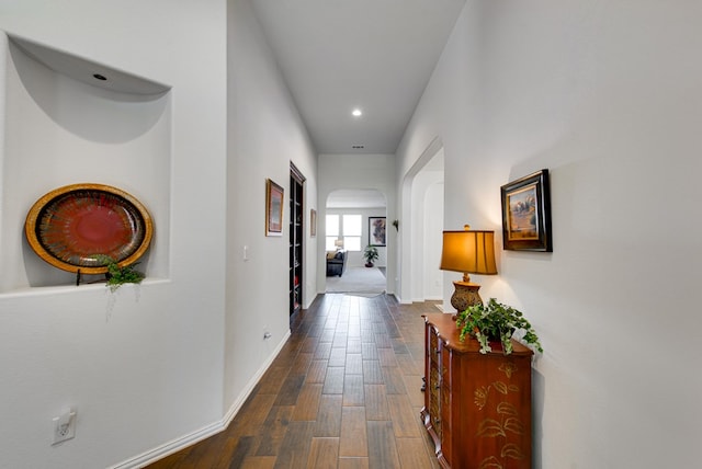 hallway with dark wood-type flooring, arched walkways, baseboards, and recessed lighting