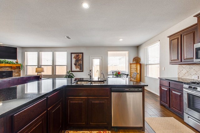 kitchen with decorative backsplash, dark wood-type flooring, stainless steel appliances, a fireplace, and a sink