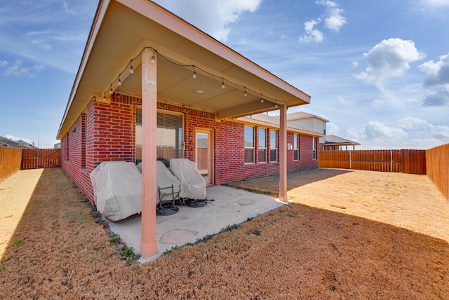 rear view of property featuring brick siding, a patio area, and a fenced backyard