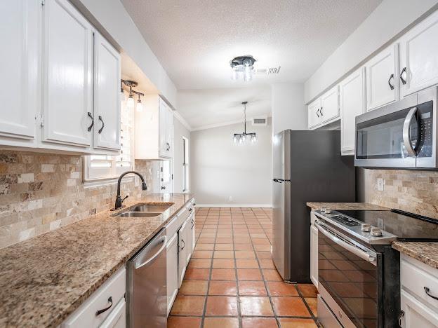 10807 E County Rd 104, Midland, TX 79706 - kitchen with appliances with stainless steel finishes, white cabinetry, tasteful backsplash, light tile patterned floors, and ornamental molding