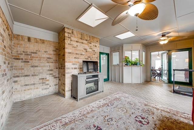 unfurnished living room with a ceiling fan, a skylight, brick floor, and brick wall