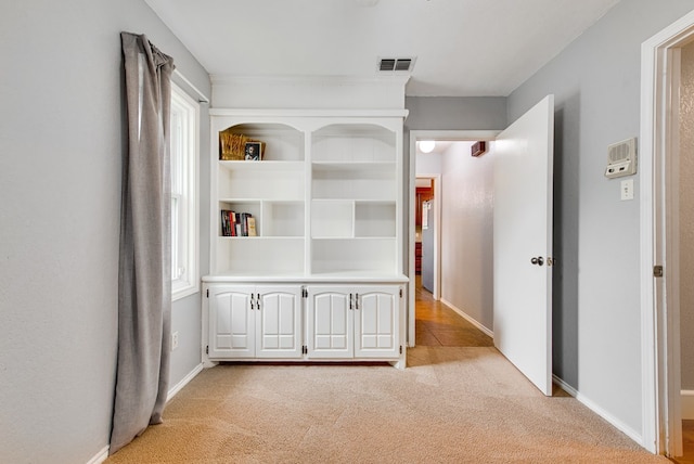 hallway with baseboards, visible vents, and light carpet
