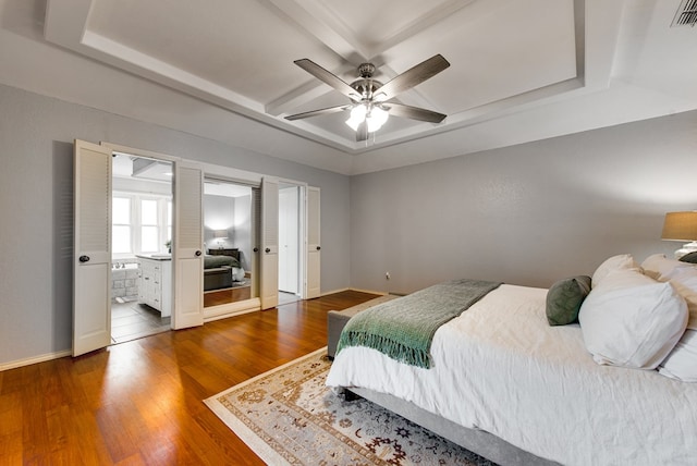 bedroom with ensuite bath, coffered ceiling, visible vents, baseboards, and wood finished floors
