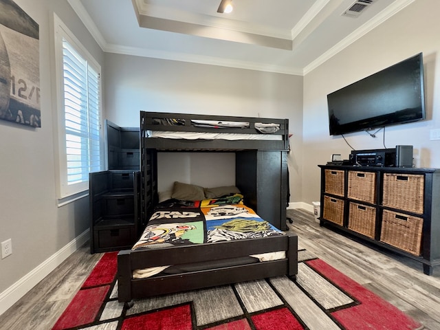 bedroom featuring hardwood / wood-style floors, ornamental molding, and a raised ceiling