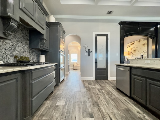 kitchen with stainless steel appliances, decorative backsplash, dark wood-type flooring, light stone countertops, and crown molding