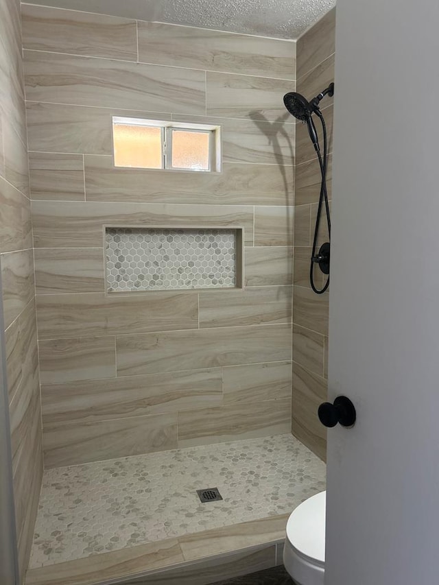 bathroom with a tile shower and toilet