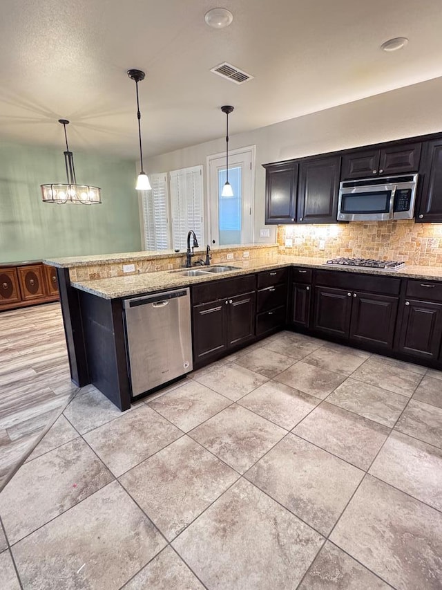 kitchen with decorative light fixtures, stainless steel appliances, light stone counters, and sink