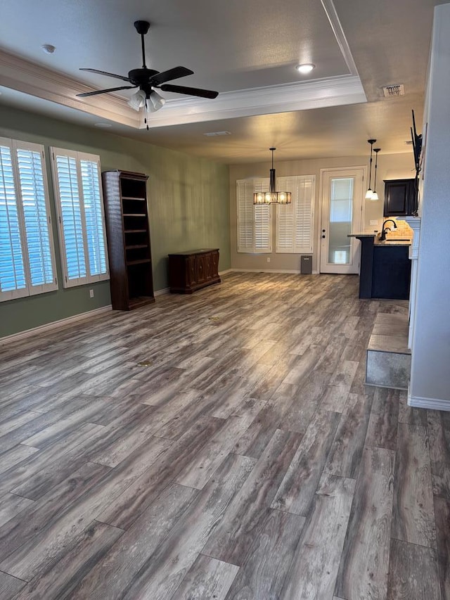 unfurnished living room featuring a raised ceiling, dark wood-type flooring, ceiling fan with notable chandelier, and ornamental molding