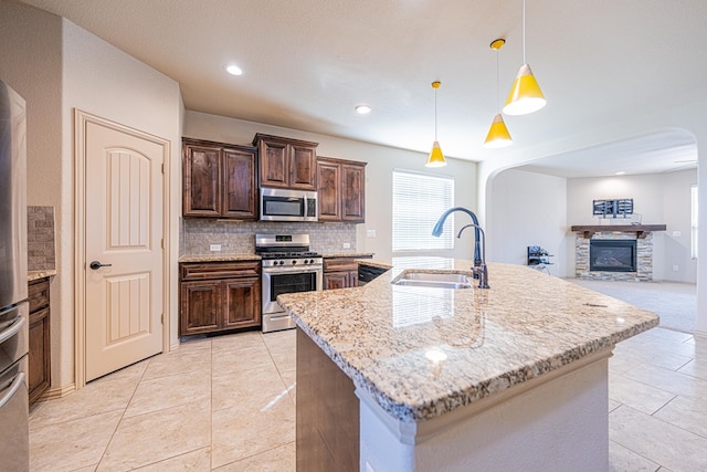 kitchen featuring light stone counters, a fireplace, a sink, appliances with stainless steel finishes, and tasteful backsplash