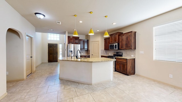 kitchen with stainless steel appliances, visible vents, backsplash, a sink, and light stone countertops