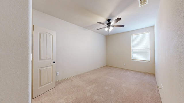 carpeted empty room with a textured wall, visible vents, and a ceiling fan