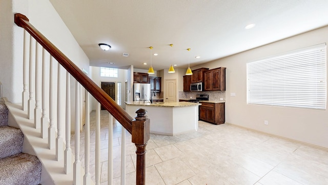 kitchen featuring appliances with stainless steel finishes, light stone counters, decorative light fixtures, a kitchen island with sink, and backsplash