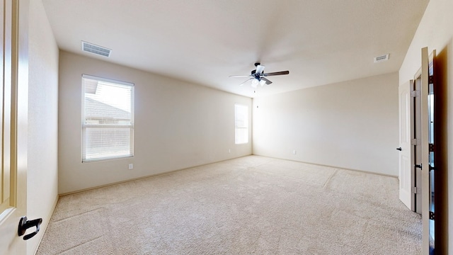 carpeted empty room featuring ceiling fan, plenty of natural light, and visible vents