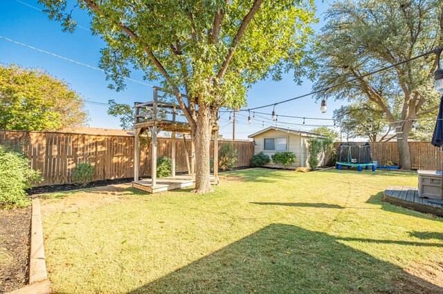 view of yard with a trampoline, an outbuilding, and a fenced backyard