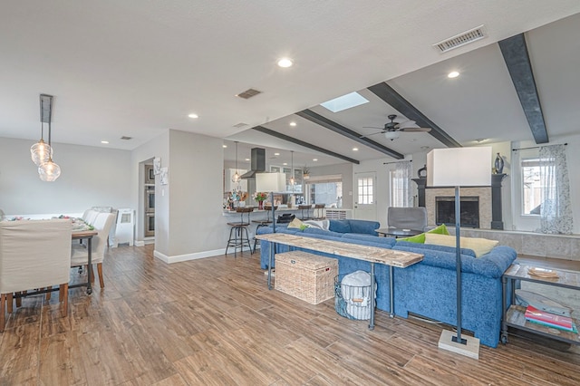 living room featuring wood finished floors, beam ceiling, a tile fireplace, and visible vents